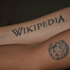 Deux bras tatoués côte à côte. Le premier, en haut, représente le texte Wikipédia, le second, en dessous, le logo de l'encyclopédie.